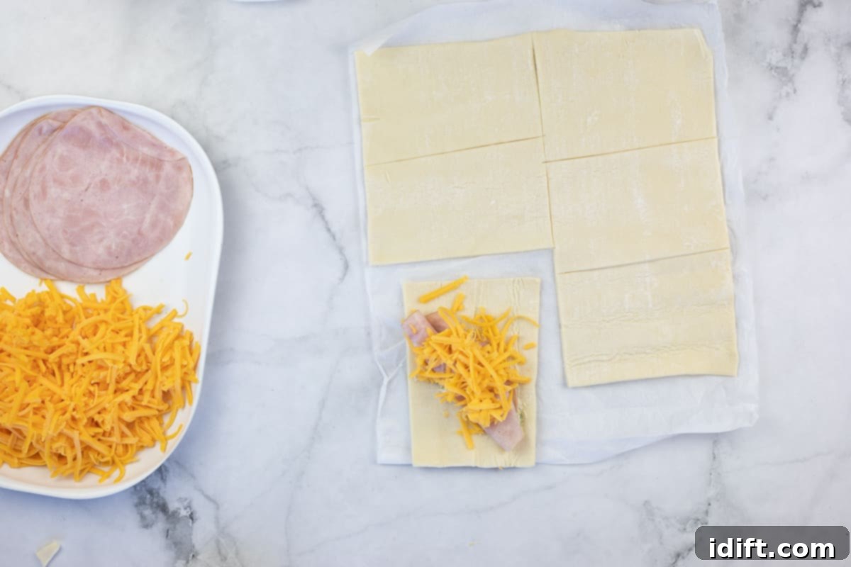 Puff pastry squares being filled with the sauce, ham, and cheese mixture.