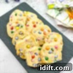 Spring Blossom Shortbread with Cheerful Candy Drops 12 Easter shortbread cookies with mini m&ms on a black plate.
