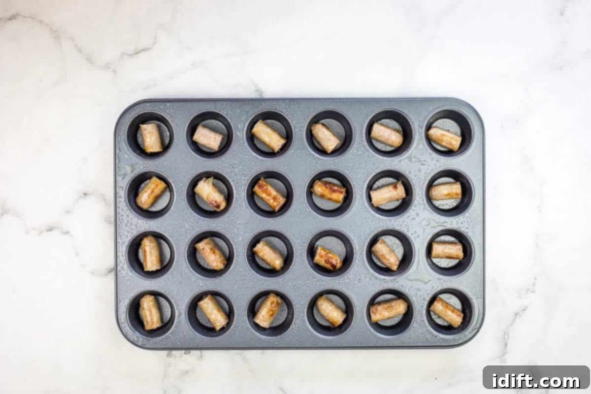 Sausage Pancake Poppers 12 Small pieces of cooked sausage placed at the bottom of each cup in a mini muffin tin.