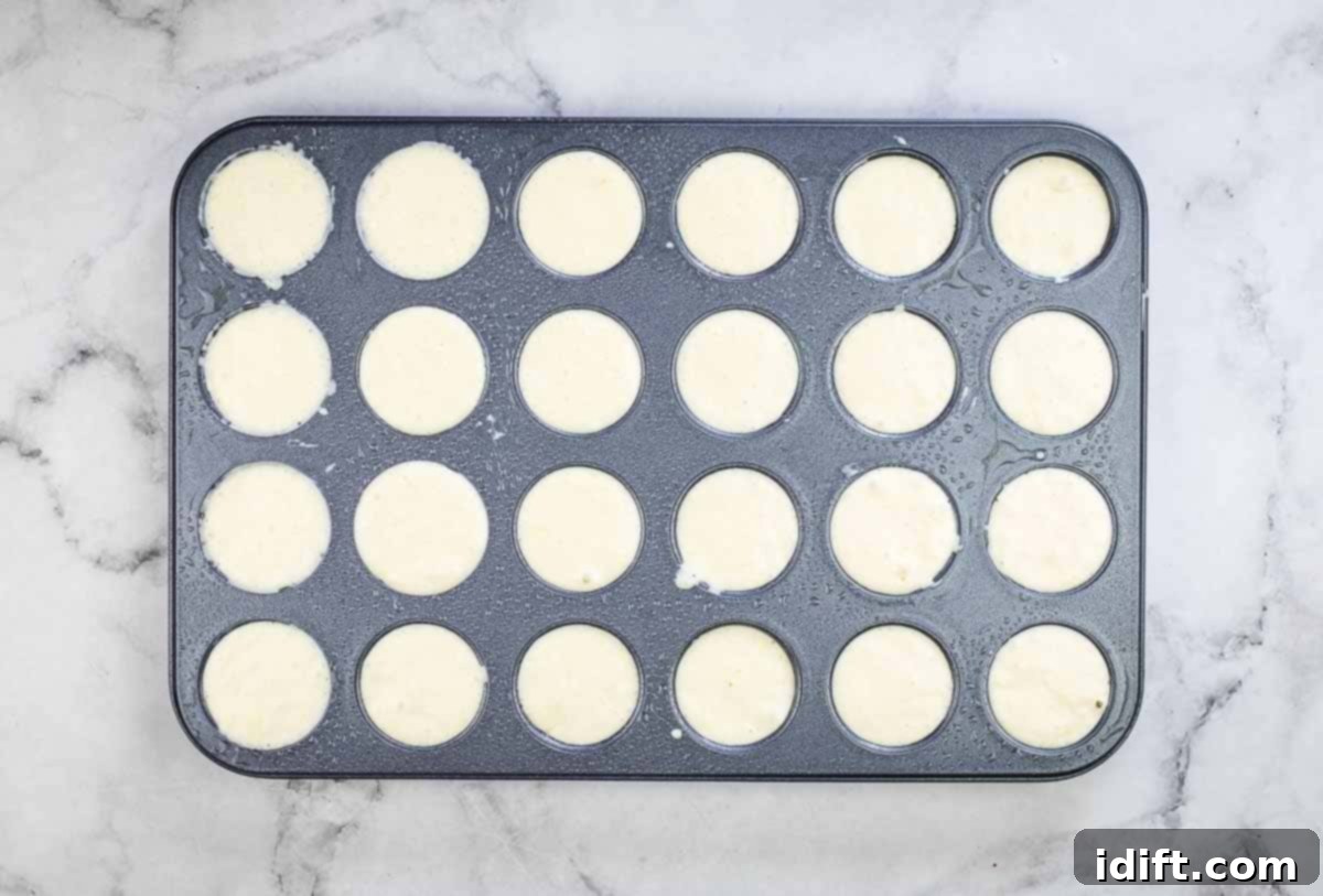 Sausage Pancake Poppers 13 Muffin tin with cups filled with pancake batter over the sausage pieces, ready for baking.