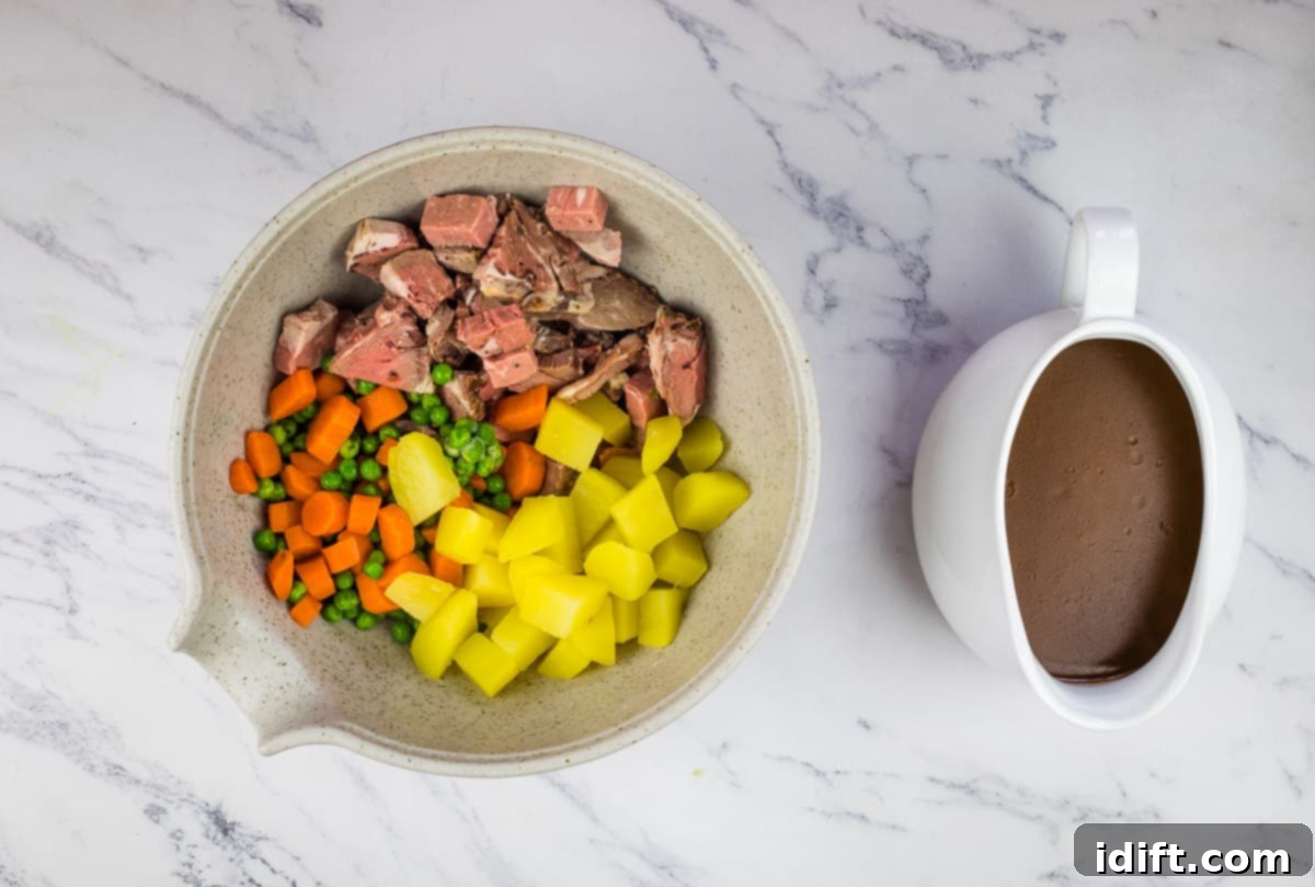 Cubed roast beef, potatoes, and mixed vegetables arranged in a bowl, ready to be tossed with gravy for the pie filling.