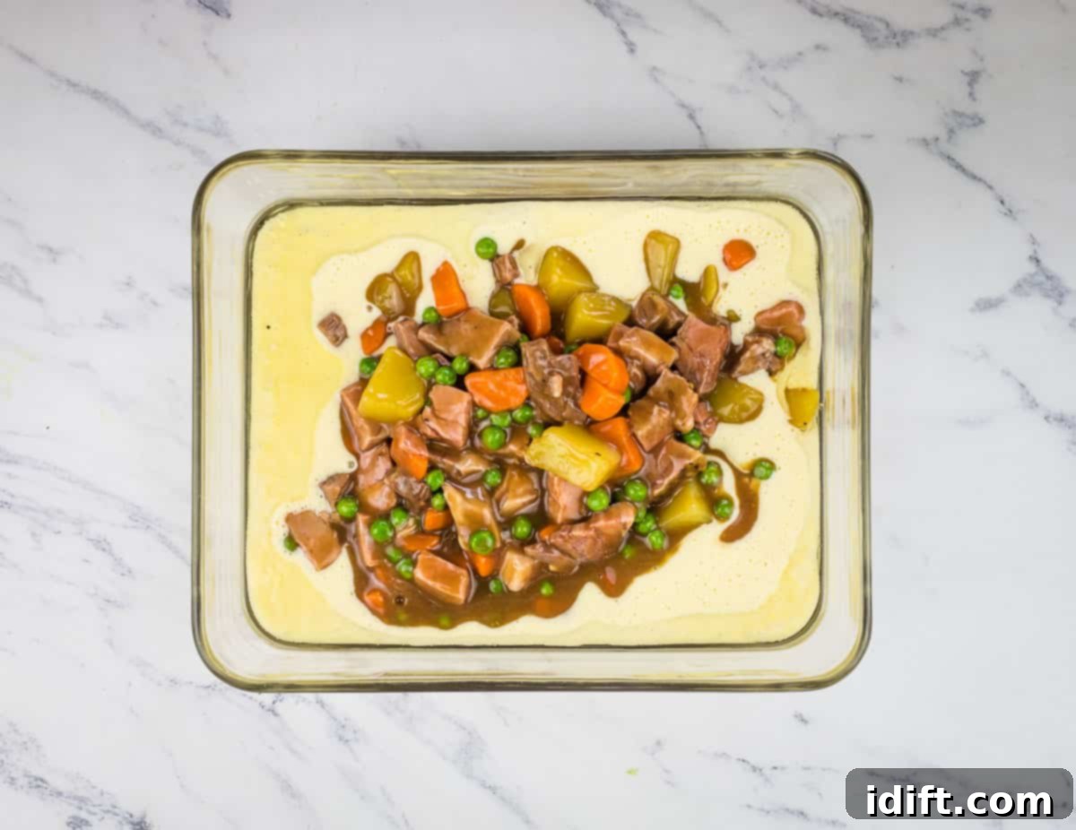 The savory roast beef and gravy mixture being spooned into the center of the Yorkshire pudding batter in the baking dish, ready for baking.