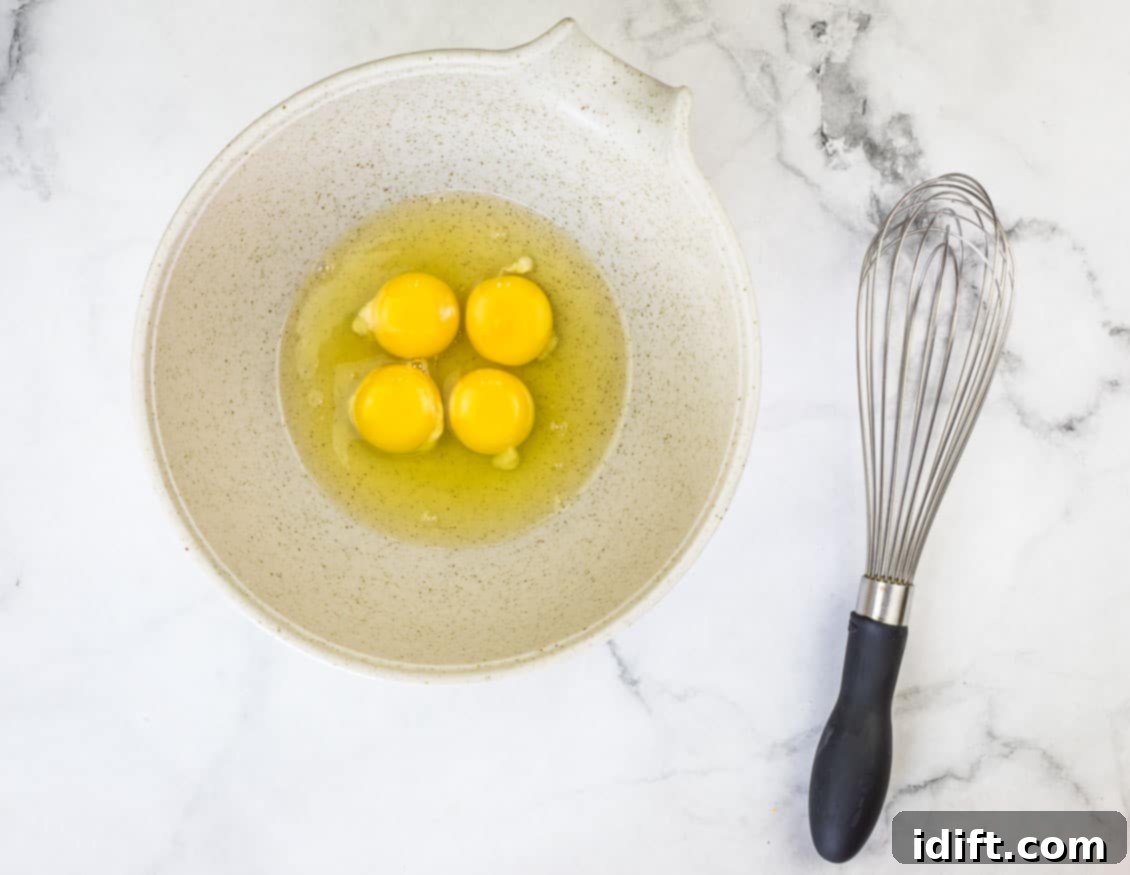 Impossible Broccoli Three-Cheese Quiche 9 A bowl of fresh eggs being whisked vigorously with a wire whisk, preparing the base for the quiche custard.