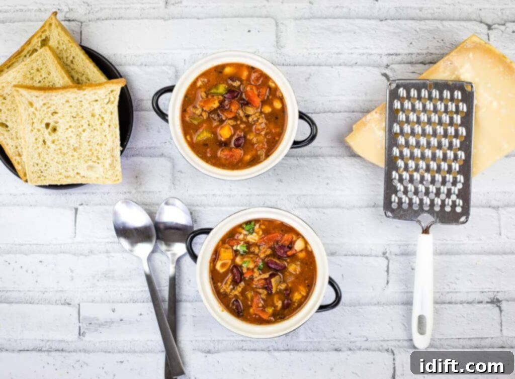 A top down shot of Pasta e Fagioli Soup with grated Parmesan cheese and a slice of crusty bread.