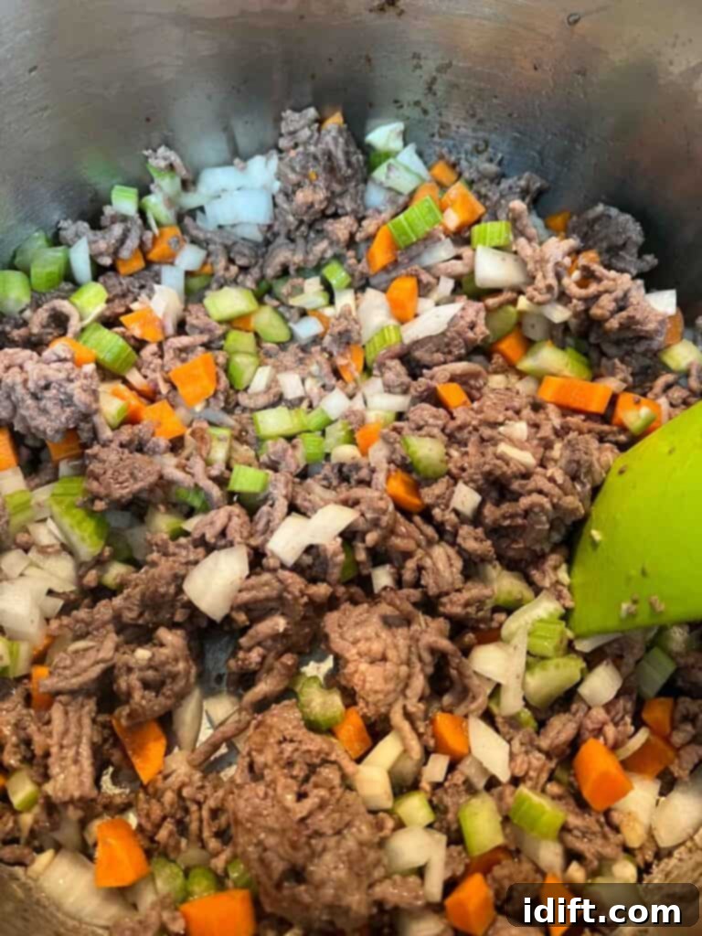 Ground beef browning in a large pot, with diced vegetables ready to be added.