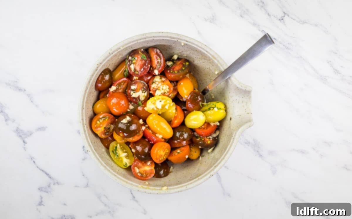 Halved tomatoes being mixed with fresh herbs, minced garlic, and olive oil in a bowl.