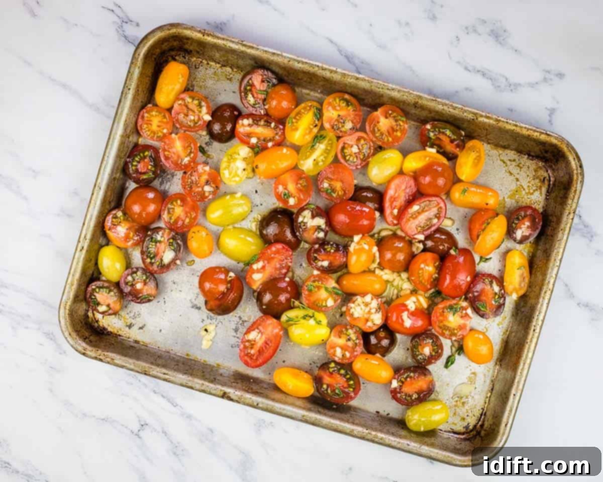 Seasoned tomatoes spread evenly on a baking sheet, ready for roasting in the oven.