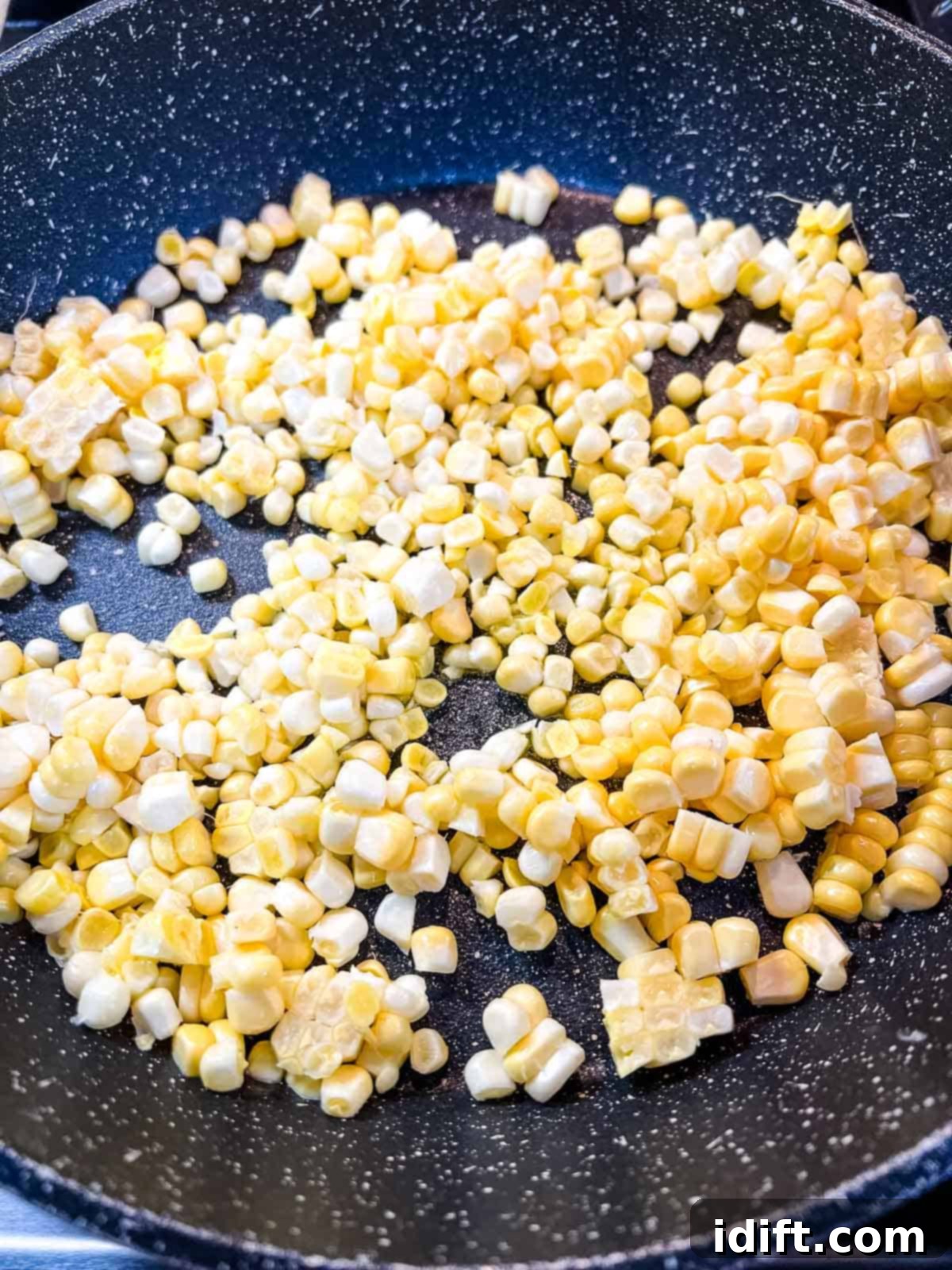Fresh corn kernels cooking in a skillet on the stovetop, gaining a brighter color.