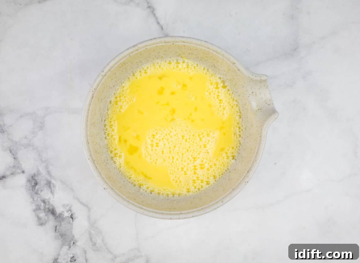 A separate bowl holding beaten eggs and apple juice, showing the liquid base for the muffins.