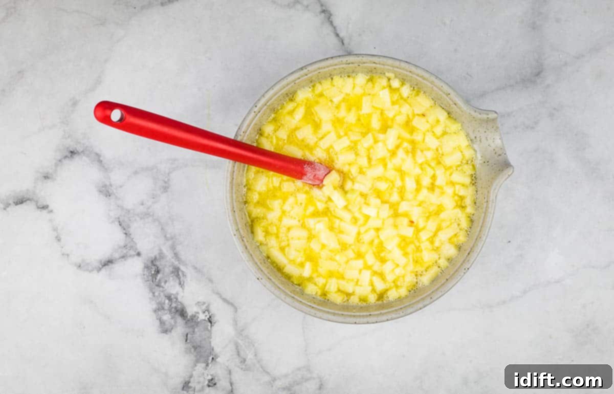 The bowl of wet ingredients now includes melted butter and finely diced apples, ready for the next step.