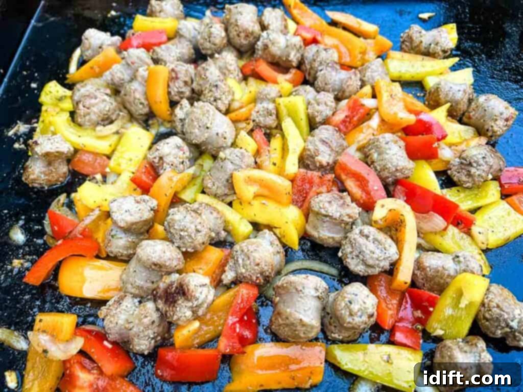 Sausage, peppers, and onions tossed together with seasoning on the griddle.