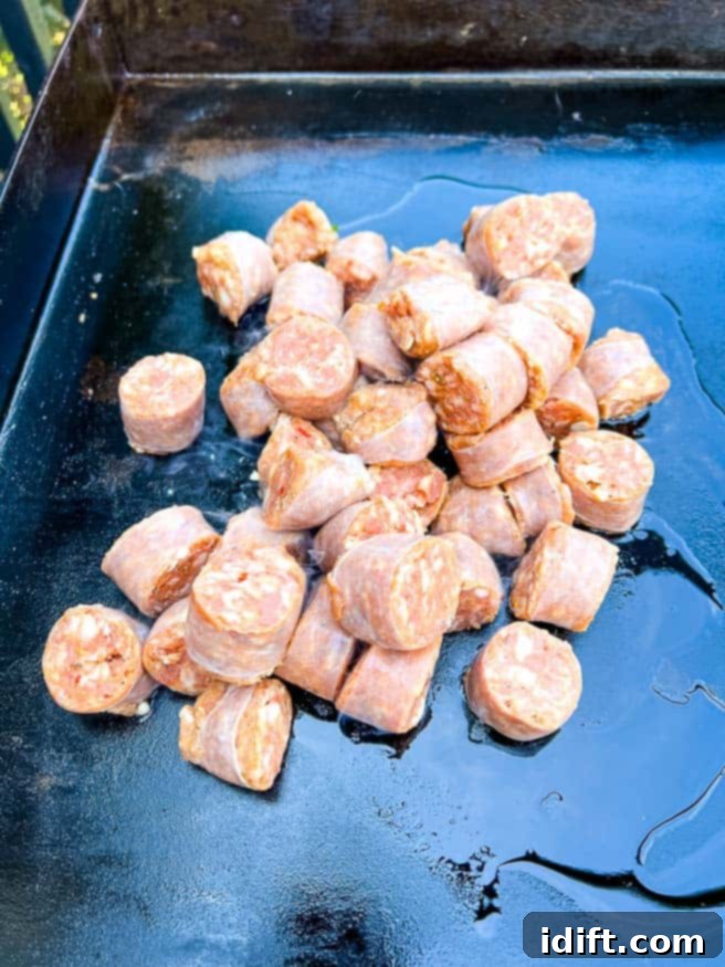 Sausage chunks cooking and browning on a hot Blackstone griddle.