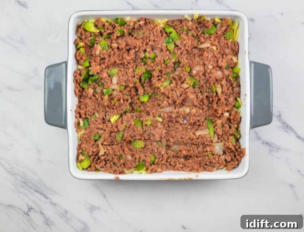 The corned beef mixture spread over the cheese layer in the casserole dish.