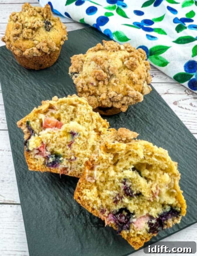 Vibrant Blueberry Rhubarb Muffins 2 Beautifully baked Blueberry Rhubarb Muffins with streusel topping, one sliced open to reveal fruit inside, presented on a plate.