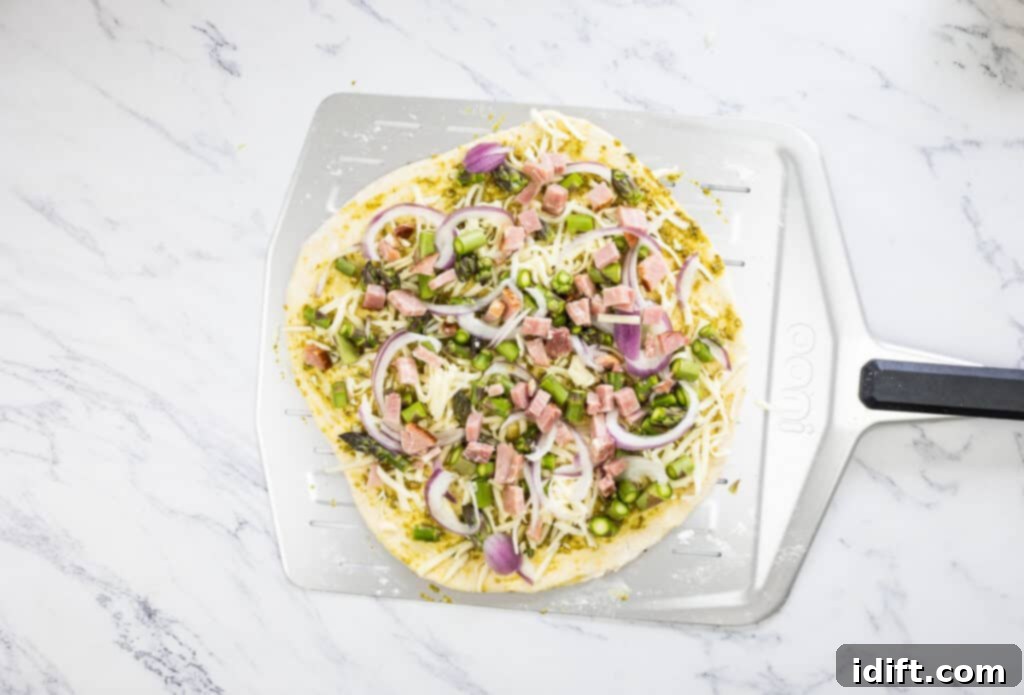 Asparagus and Prosciutto Masterpiece 11 Pizza topped with diced ham and sliced red onion, ready for the oven.