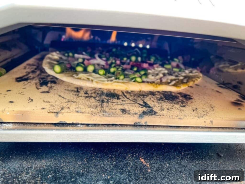 Asparagus and Prosciutto Masterpiece 12 Pizza cooking inside the Ooni oven, showing the flame and browning crust.