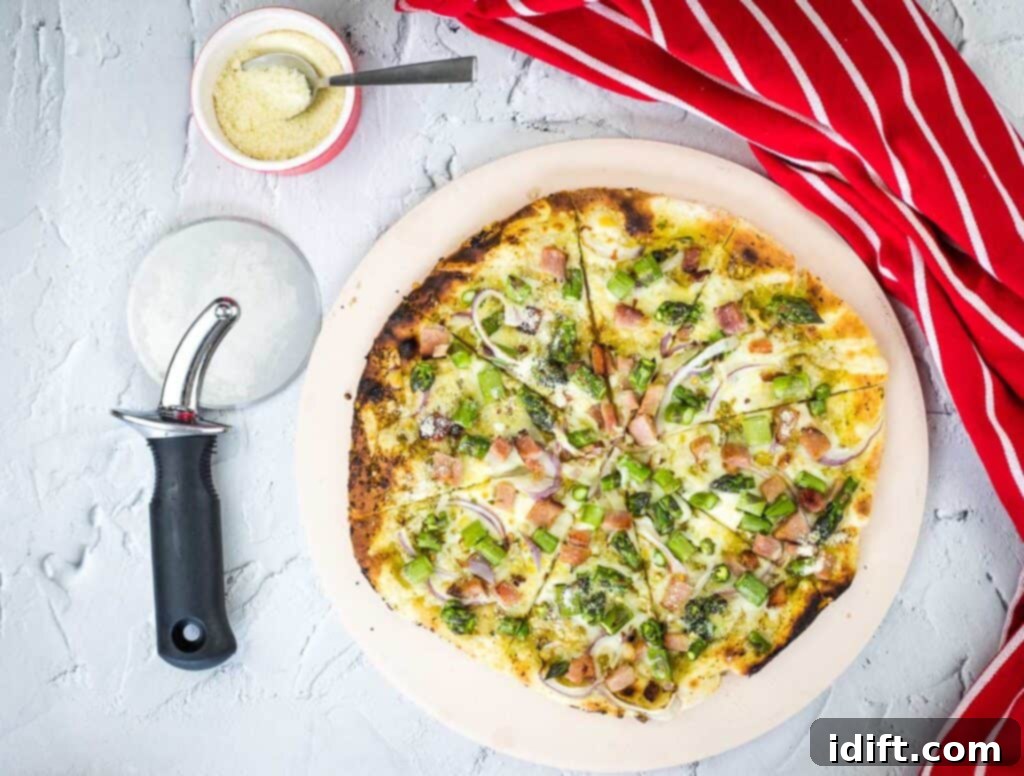 Asparagus and Prosciutto Masterpiece 3 A horizontal shot of a freshly sliced Ham and Asparagus Pizza, with a pizza cutter and scattered cheese nearby, ready to be served.