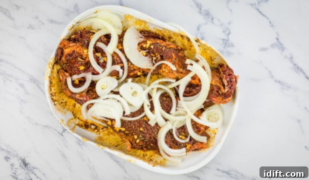 Tender Hanger Steak with Bright Chimichurri 10 Sliced onions and garlic cloves placed on top of the rubbed hanger beef before marinating.