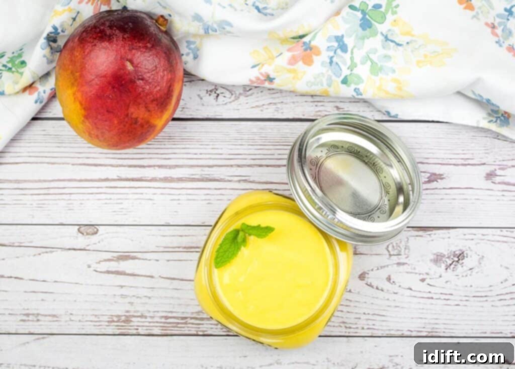 Mango curd in a glass jar, with a fresh whole mango and cut mango slices beside it.