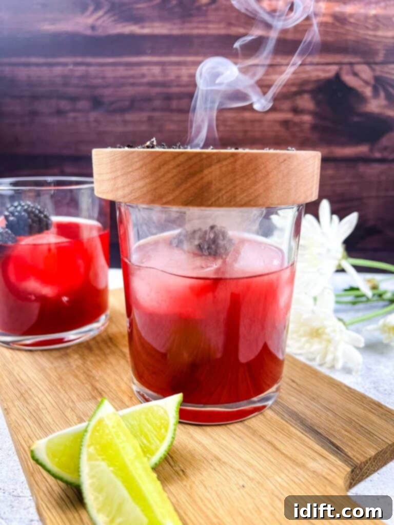 A finished Smoked Blackberry Margarita with the smoking plate still covering the glass, filled with aromatic smoke.