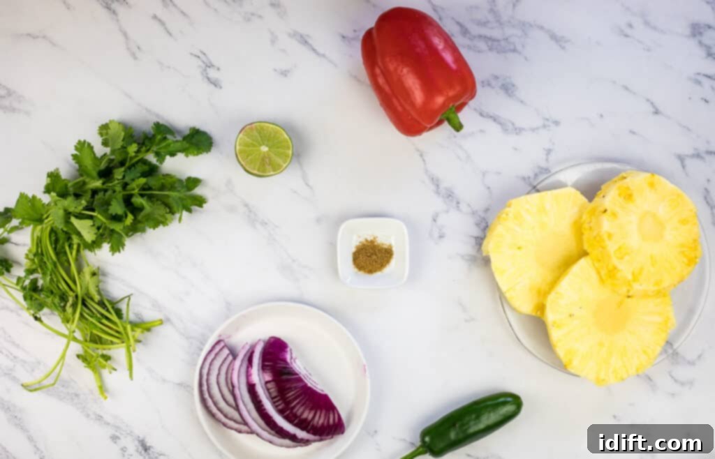 Fresh ingredients for the grilled pineapple salsa laid out on a cutting board: pineapple slices, red bell pepper, red onion, and a whole jalapeño.