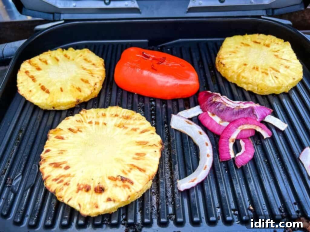 Pineapple slices, red bell pepper halves, red onion rings, and a whole jalapeño grilling on the Ninja Woodfire Grill grates, developing char and smoky flavor.
