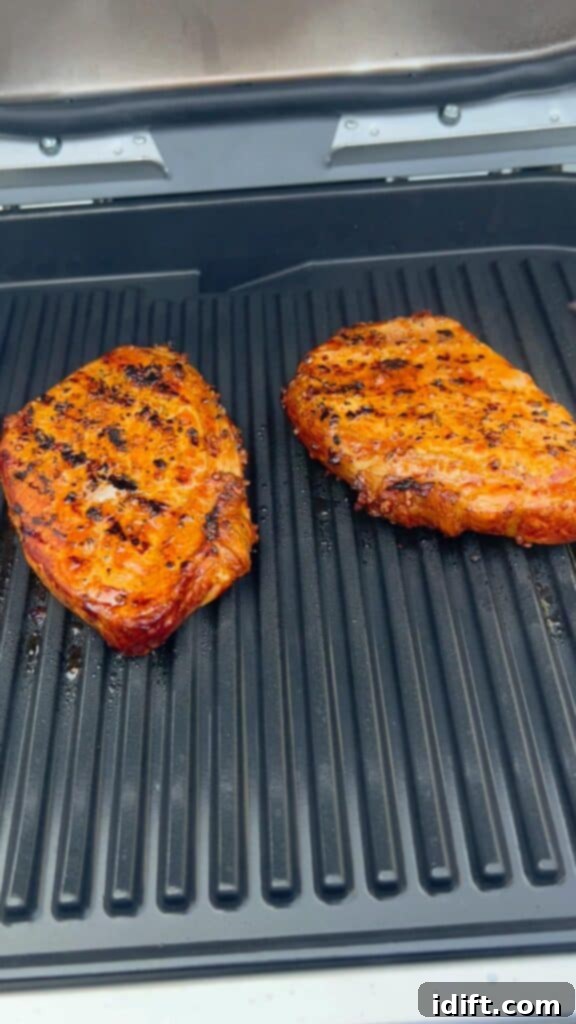 Pork chops grilling on the Ninja Woodfire Grill, enveloped in flavorful smoke, with clear grill marks forming.
