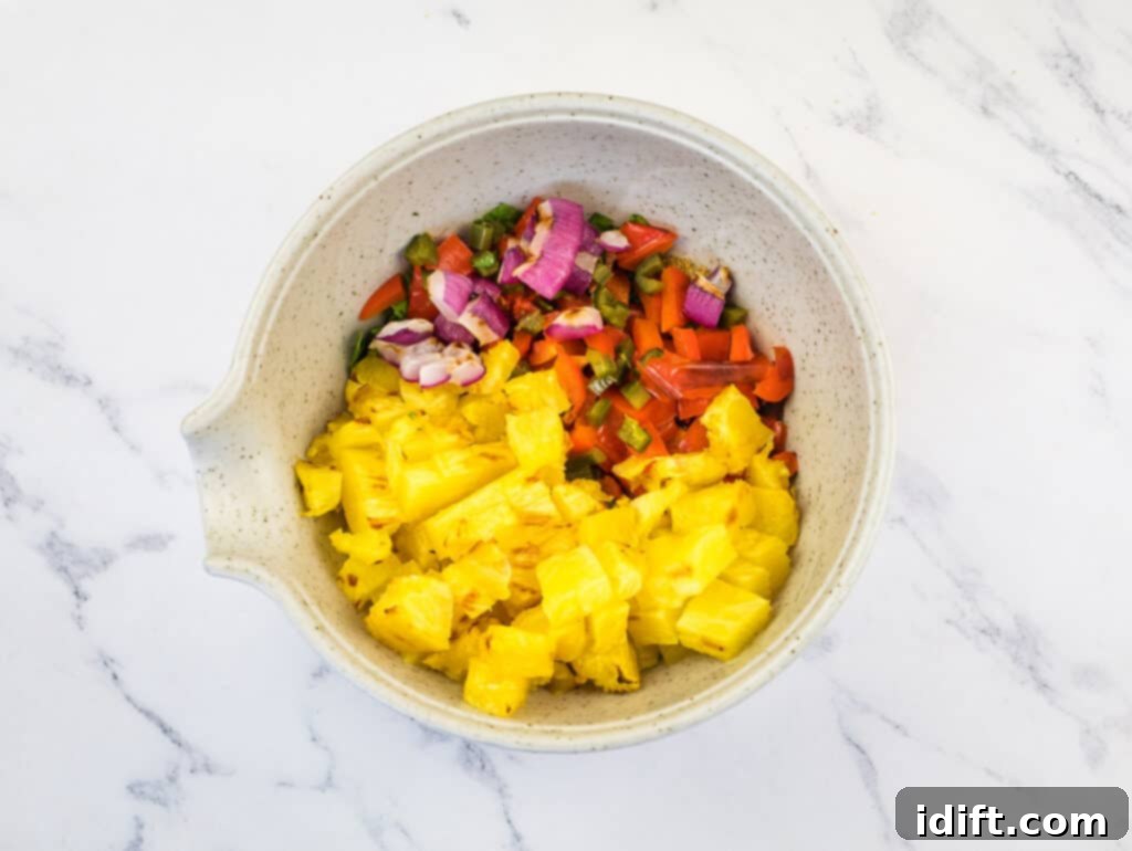 All grilled pineapple salsa ingredients (diced pineapple, bell pepper, onion, jalapeño) in a bowl, ready to be mixed with cilantro and lime.