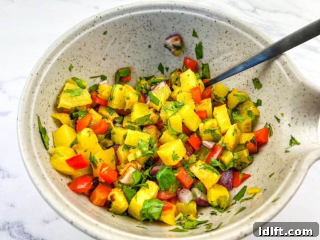 The finished grilled pineapple salsa, a colorful mix of diced fruit and vegetables, stirred in a bowl with a spoon.