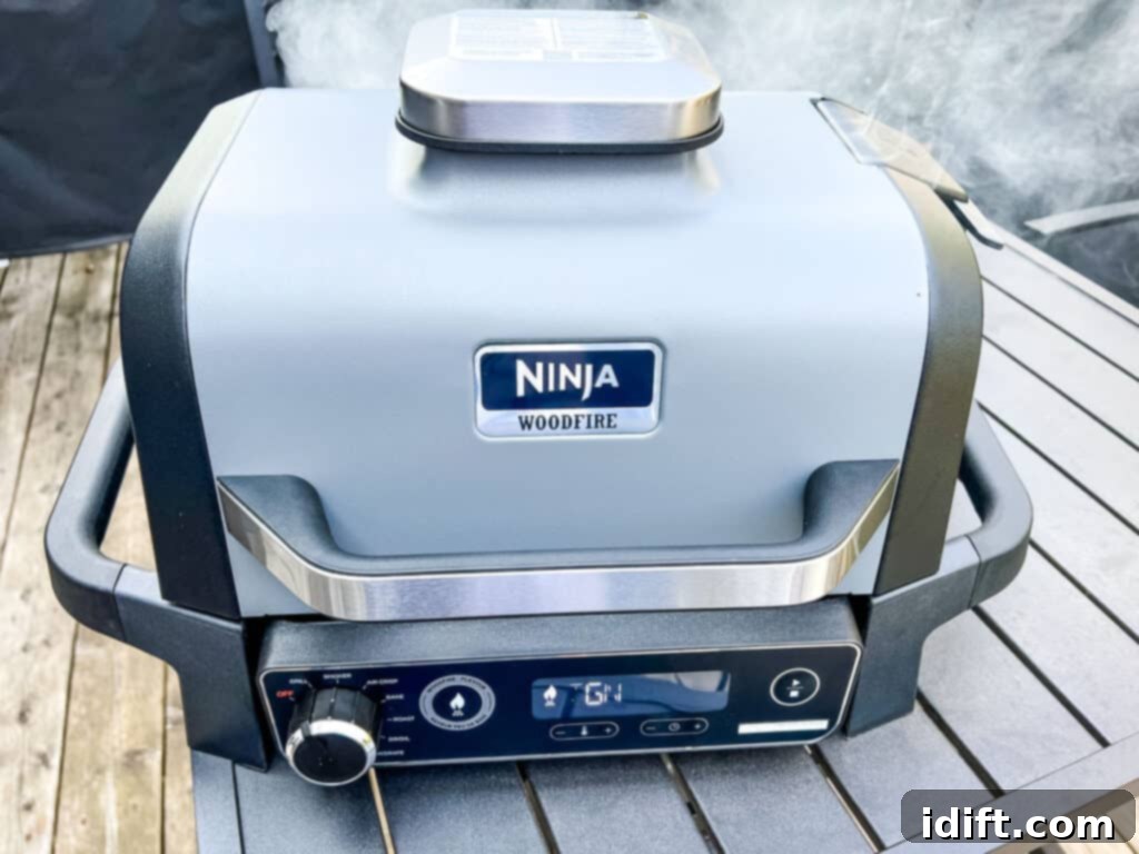 A close-up image of a closed Ninja Woodfire Grill, actively emitting smoke, indicating the woodfire flavor feature is engaged.