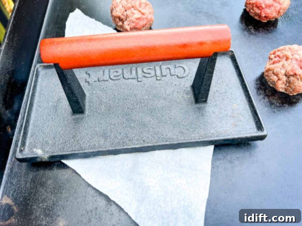 Griddle Gold: The Art of the Blackstone Smash Burger 5 A chef's hand pressing down a meatball with a burger press and parchment paper to create a smash burger.