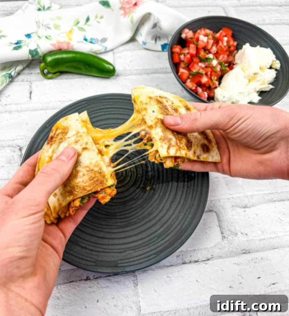 Two hands pulling apart a Chicken Al Pastor Quesadilla, revealing melted cheese and seasoned chicken.