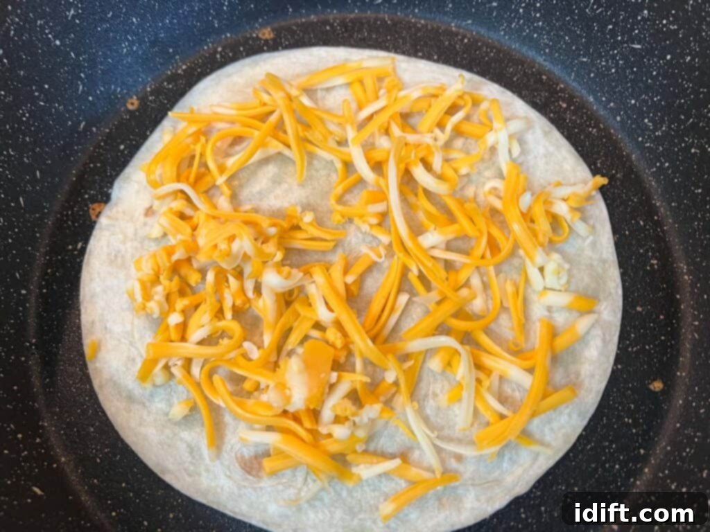 The first tortilla is placed in a skillet and topped with a layer of shredded cheese.