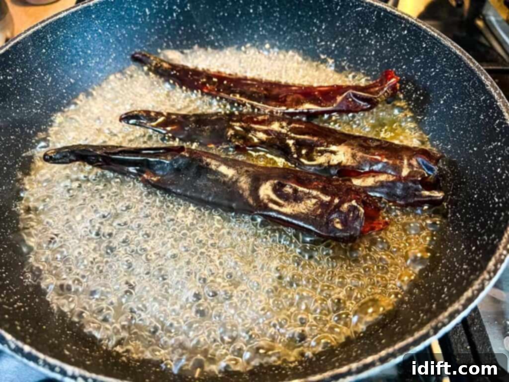 Toasted guajillo chiles softening in water in a skillet.