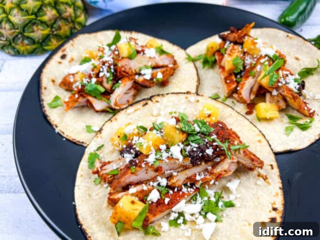 Close-up of Smoked Chicken Al Pastor Tacos served on a black plate, garnished with cilantro.
