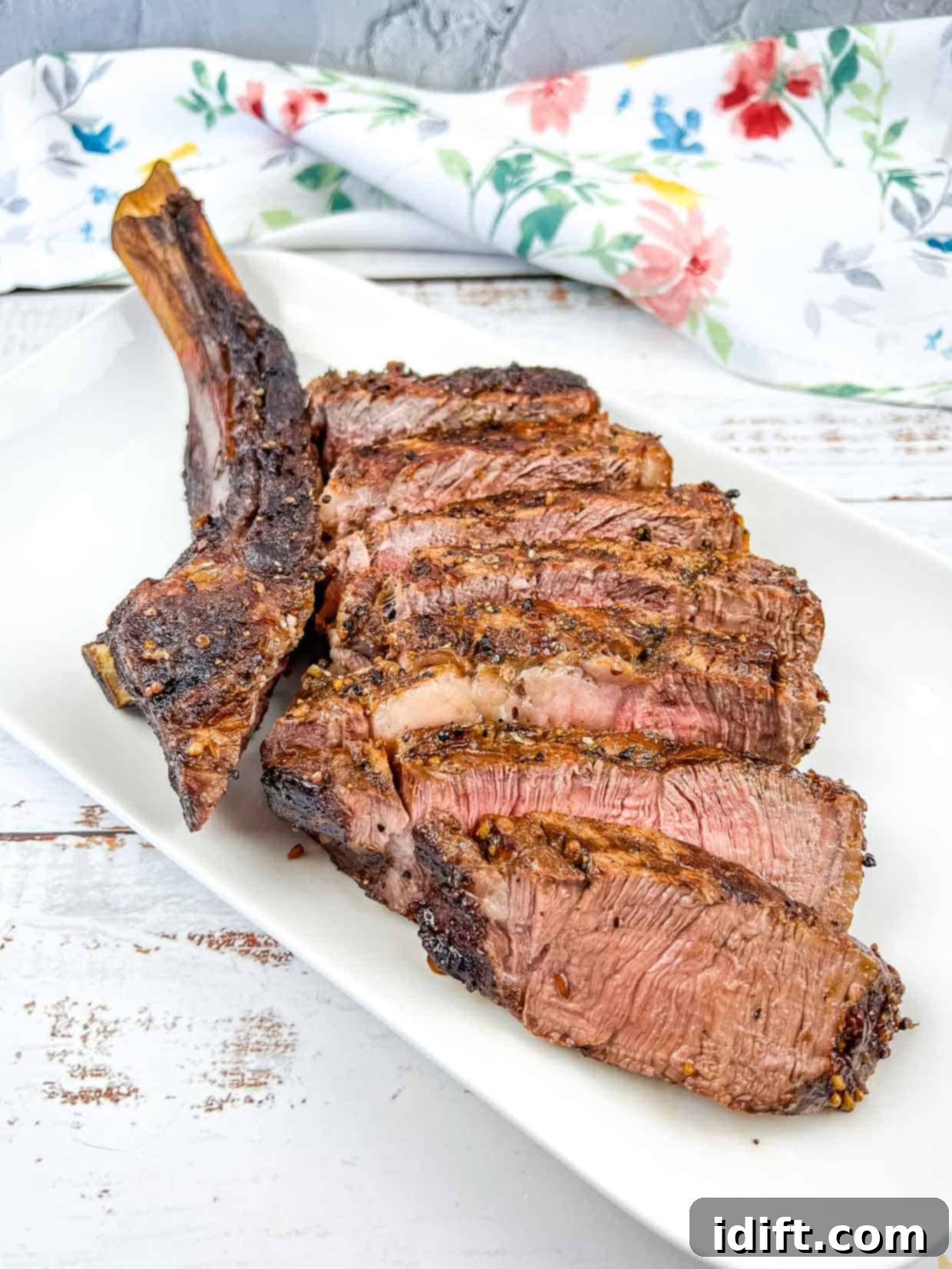 A tomahawk steak cooked on the Ninja Woodfire Grill. Sliced and served on a white platter.