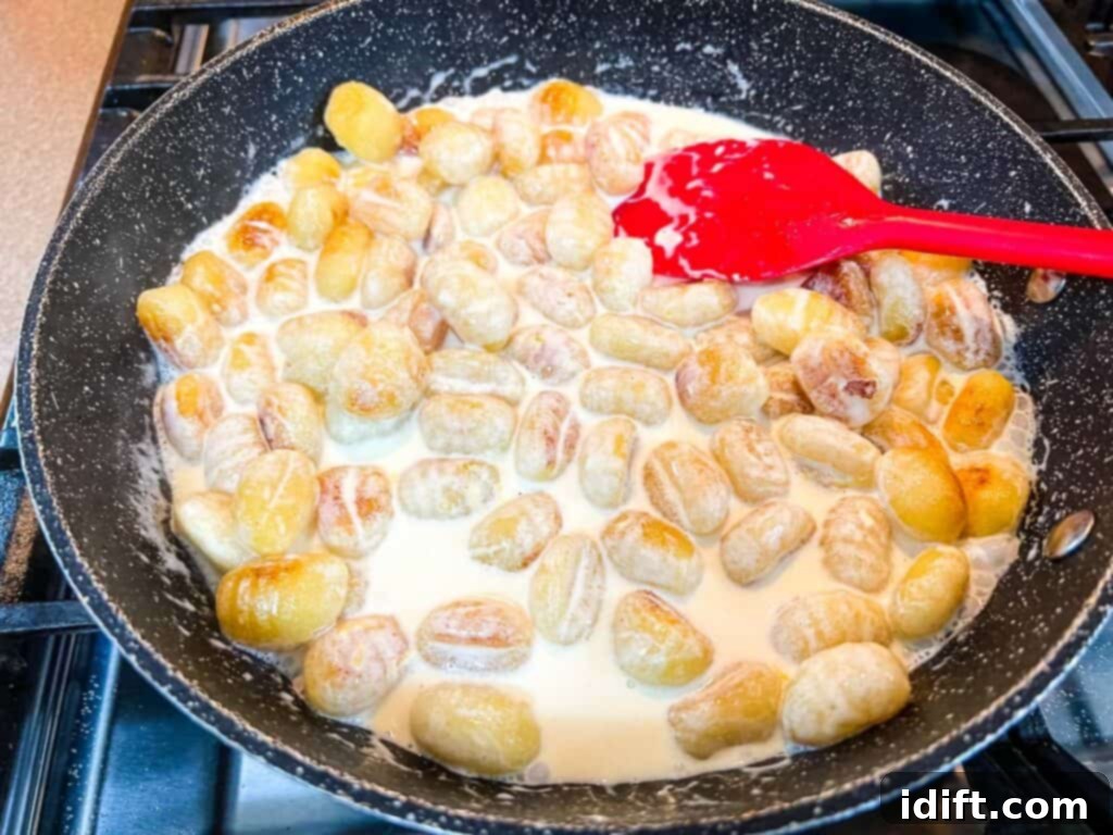 Heavy cream and grated cheese being added to the browned gnocchi in a skillet.