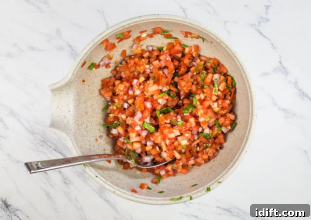 Effortless Bruschetta Bites 7 Mixed tomato bruschetta mixture in a bowl with a spoon.