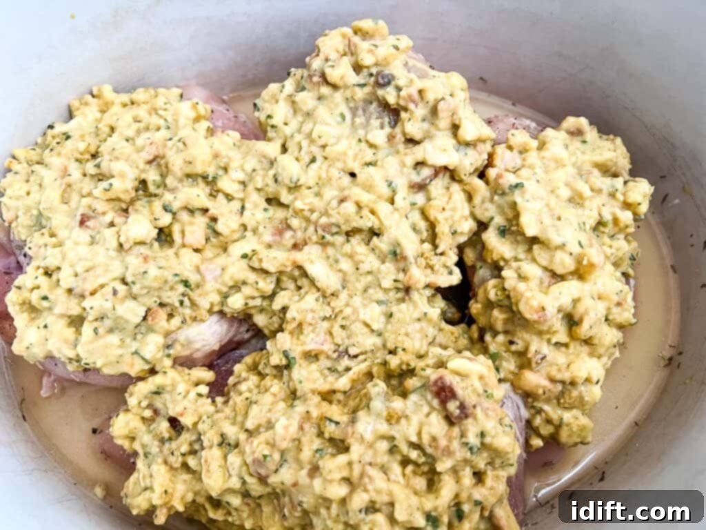 Chicken breasts in the slow cooker topped with the stuffing mixture, ready for cooking.