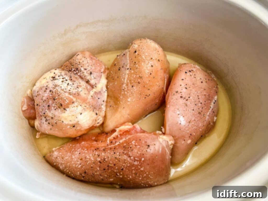 Seasoned chicken breasts in the slow cooker with liquid at the bottom.