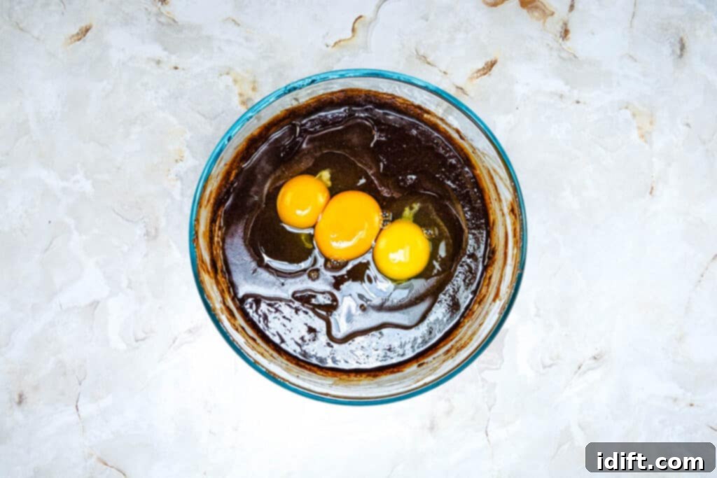 Autumn Fudgy Brownie Bites 8 Eggs being stirred into the rich, dark brownie batter, ensuring a smooth and cohesive mixture for the base of the cupcakes.