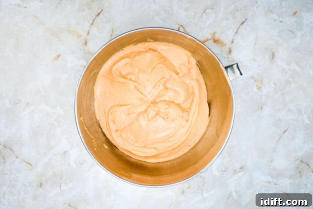 Autumn Fudgy Brownie Bites 12 Smooth vanilla cake batter vibrant orange, prepared for the top layer of the Fall Brownie Cupcakes, ready for baking.