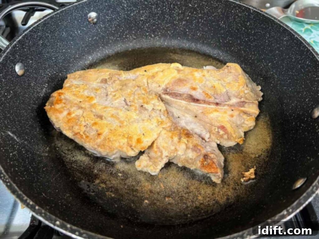 A dredged pork chop beautifully browning in a hot skillet.