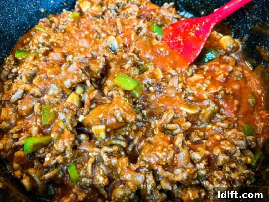 Priceless Pasta Bake 12 A skillet full of meat and sauce with a red spoon.