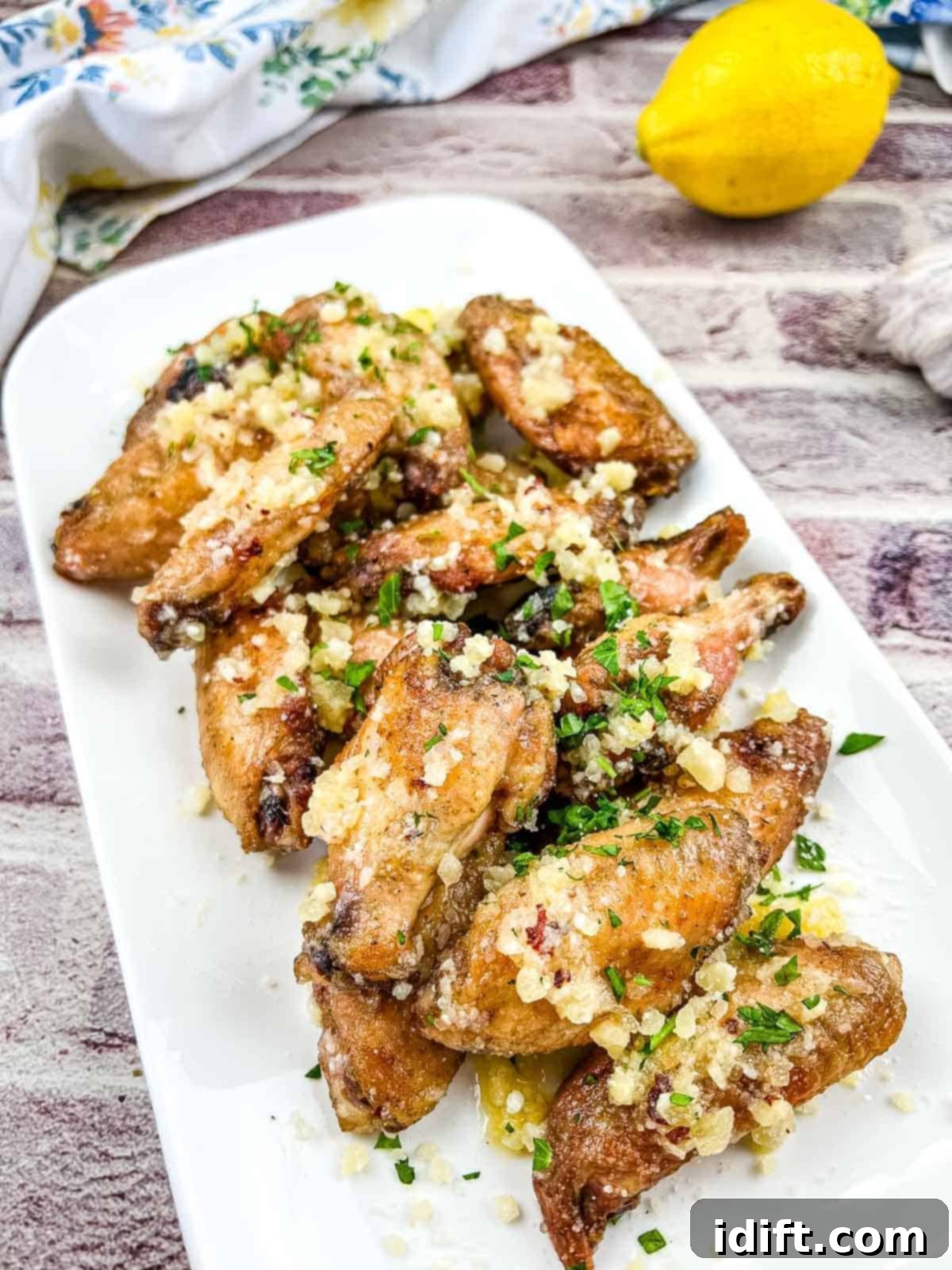 Irresistible Smoked Garlic Parmesan Wings 2 Chicken wings with lemon and garlic on a white plate.