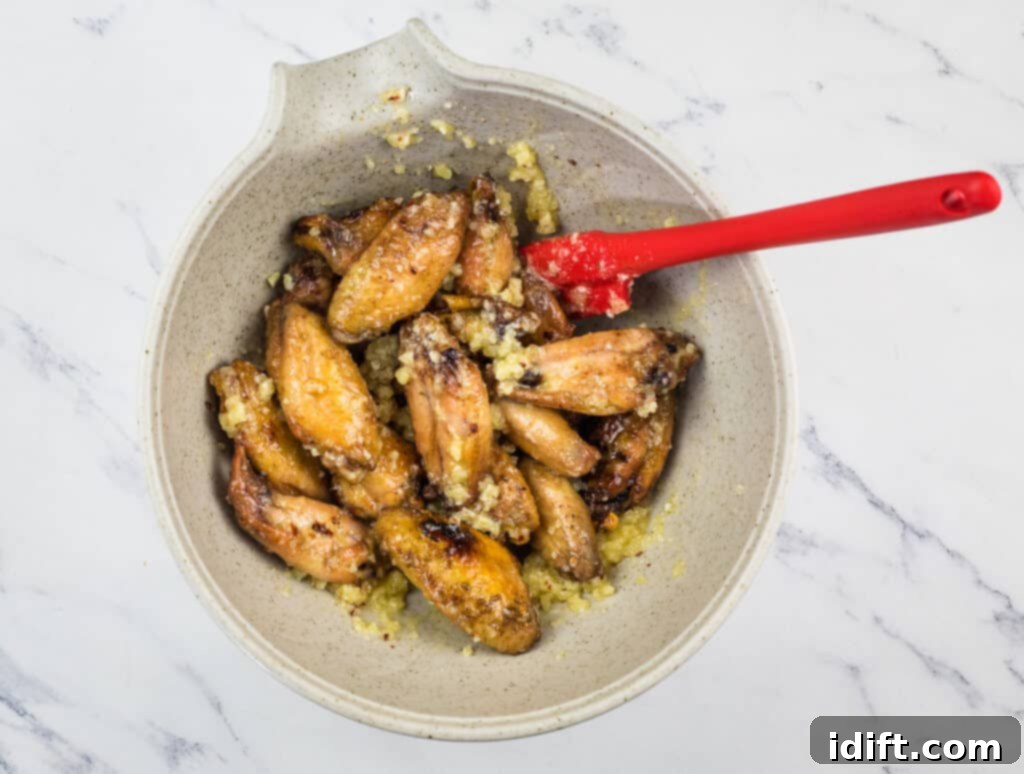 Irresistible Smoked Garlic Parmesan Wings 10 Chicken wings in a bowl with a red spoon.