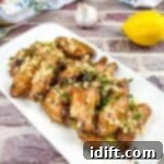 Irresistible Smoked Garlic Parmesan Wings 11 Chicken wings with lemon and garlic on a white plate.