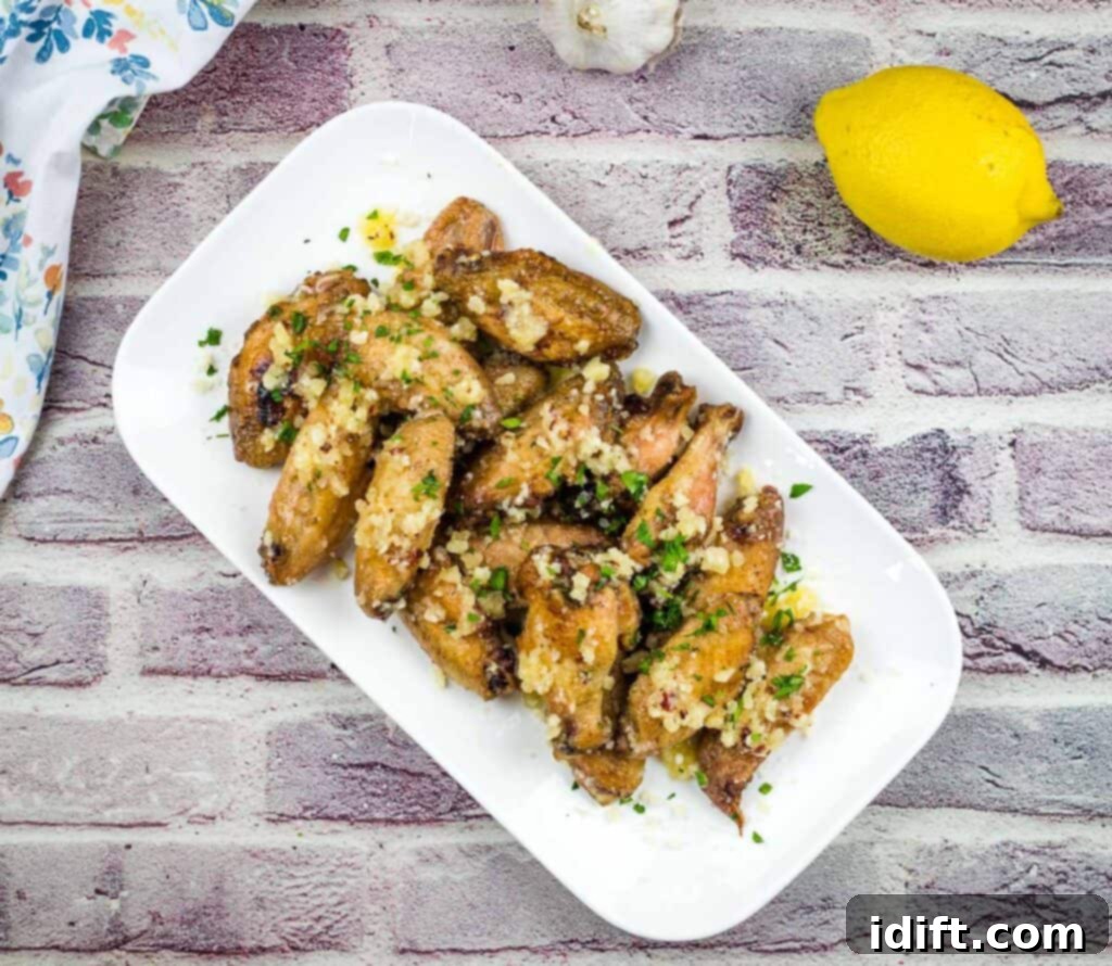 Irresistible Smoked Garlic Parmesan Wings 3 Chicken wings with garlic and lemon on a white plate.