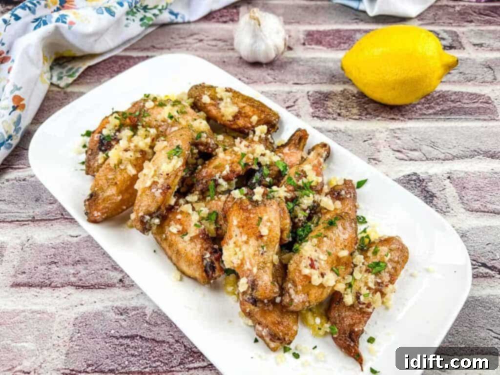 Irresistible Smoked Garlic Parmesan Wings 5 Chicken wings with lemon and garlic on a white plate.