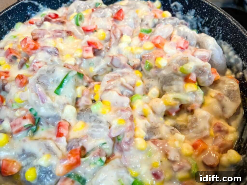 Comforting Baked Shrimp and Grits Casserole 20 A frying pan filled with cooked shrimp, corn, and peppers in a rich sauce.